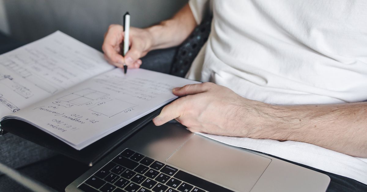 A person writing project notes beside a laptop